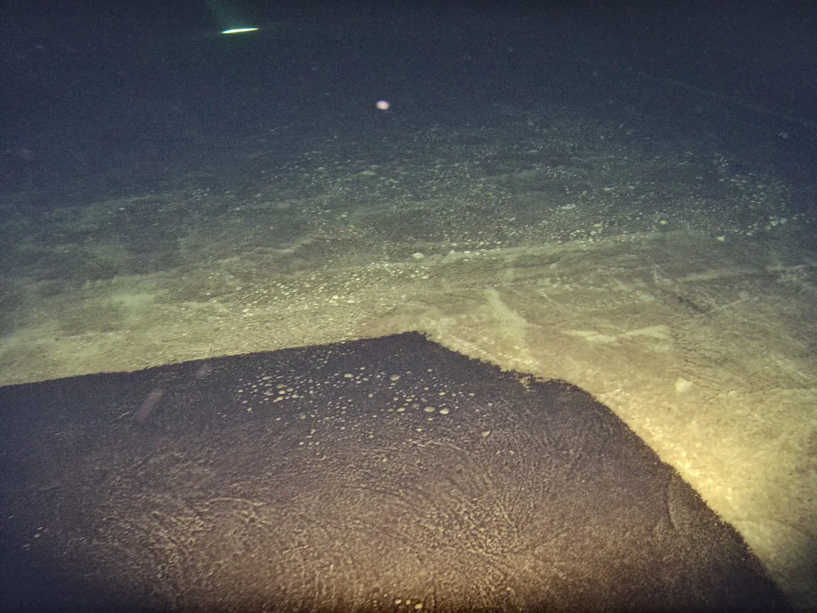 Underwater reservoir floor with a clear boundary between dark and light sediment.